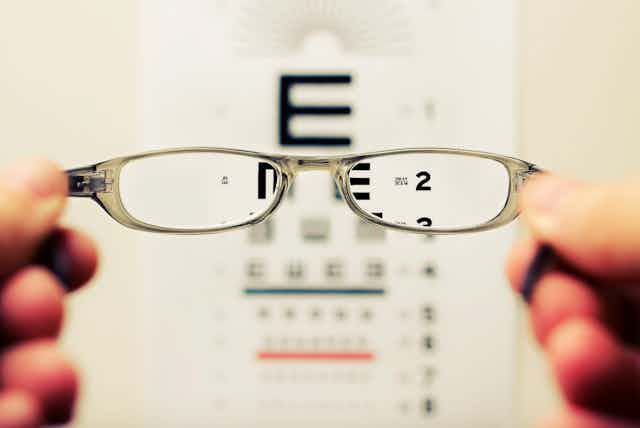 Glasses held in front of a letter chart. 