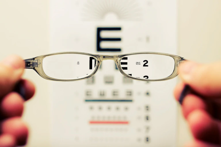 Glasses held in front of a letter chart.