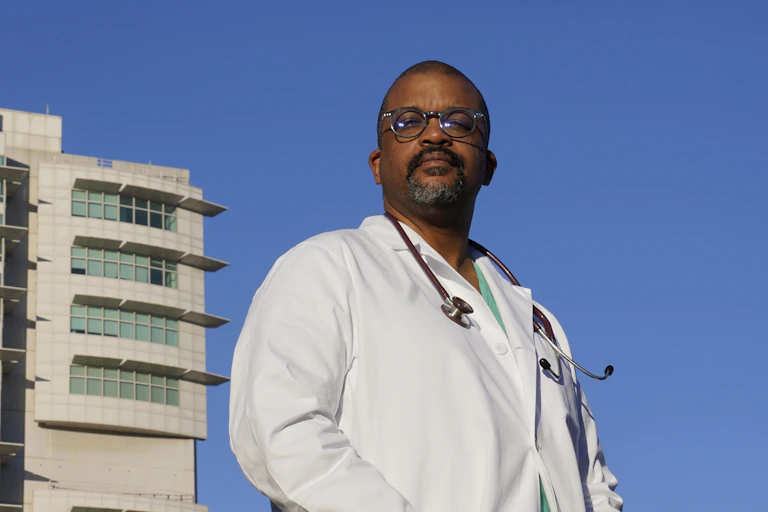 A doctor in his white coat stands in front of his hospital