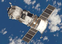 Le vaisseau spatial russe Progress flottant au-dessus de la Terre. Il est cylindrique avec deux panneaux solaires dépassant sur les côtés