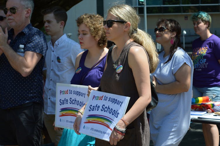 Two women hold signs showing support for Safe Schools program