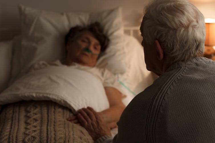 Elderly man holding sick wife's hand