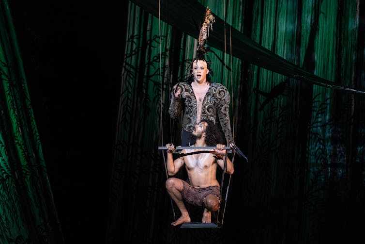 Production image; two men sing on a swing