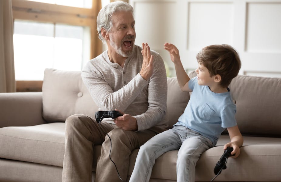 A man with grey hair high fiving a young boy, both holding controllers for a video game.