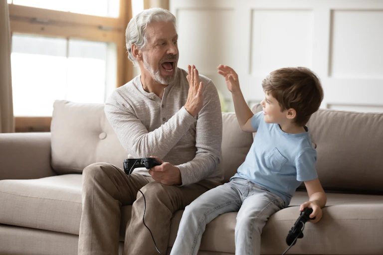 A man with grey hair high fiving a young boy, both holding controllers for a video game.