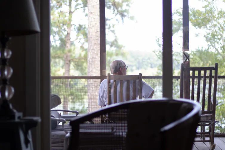 Man sits on chair on balcony looking out at woods