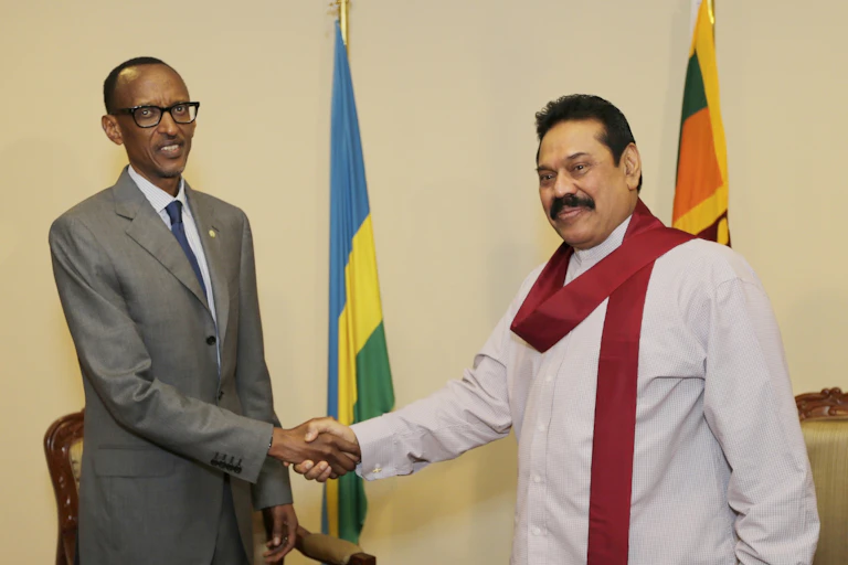A black man in a suit shaking hands with a brown man in traditional Sri Lankan garb