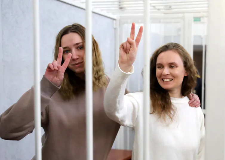 Katerina Bakhvalova and Daria Chultsova in a cage making two-fingered peace gestures.
