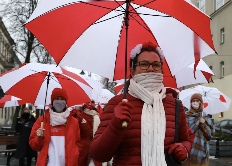 Women in the street dressed in red and white and holding up red and white umbrellas.