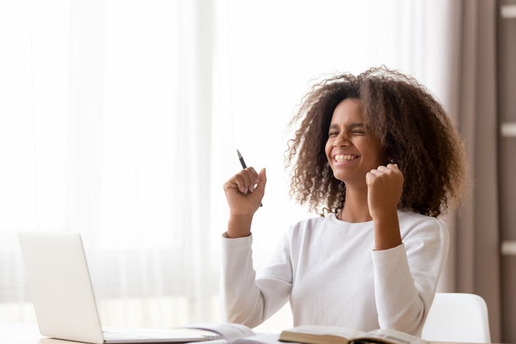 Une jeune étudiante assise à son bureau est heureuse après avoir reçu de bonnes nouvelles