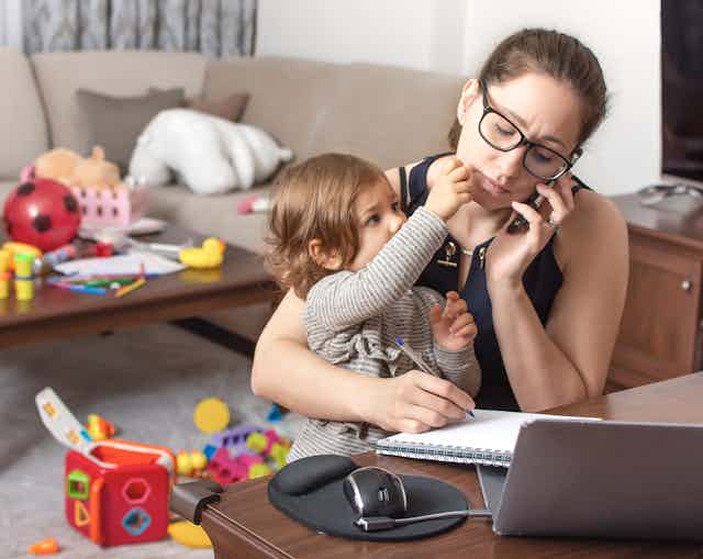 A woman working at home and caring for her child.