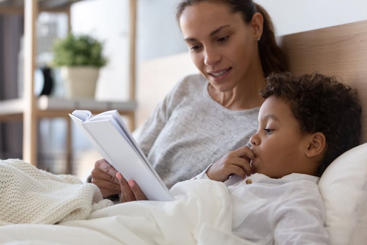 A woman reads to a child in bed.