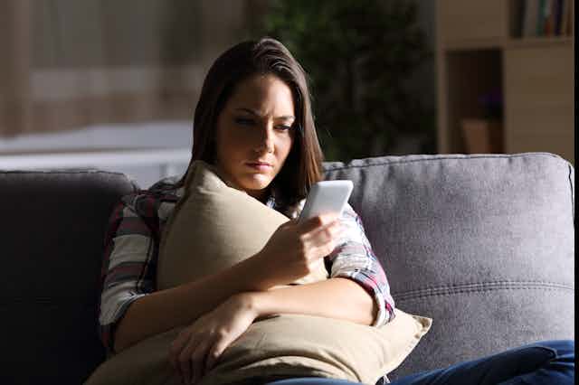 A young woman sits on the couch looking at her smartphone.