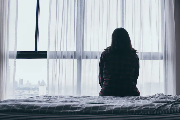 A woman sits on a bed looking out the window.