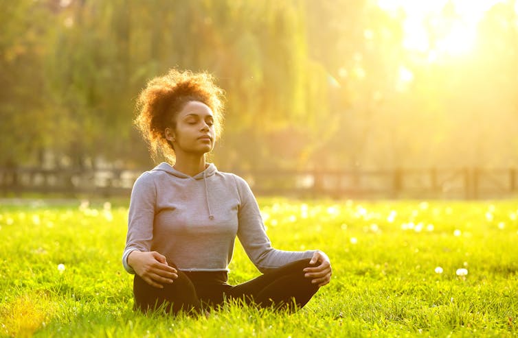 A young woman meditates in a park.