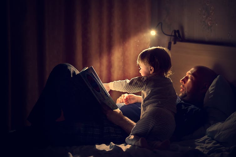 A man and a child read a book in bed.