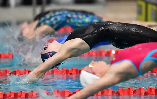 Swimmers launch backwards in the pool for the start of a race.