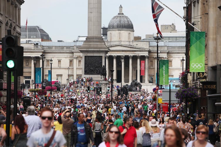Crowds of people in one of London's busy streets, Olympic banners on buildings and signs,
