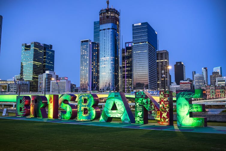 Green lights illuminate the  Brisbane sign at Southbank with the  city scape in the background.