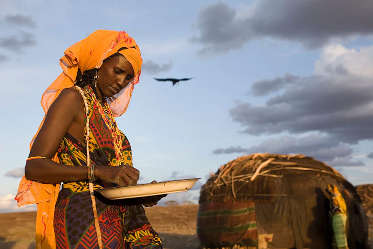 Woman sorts through maize kernels in a tray.