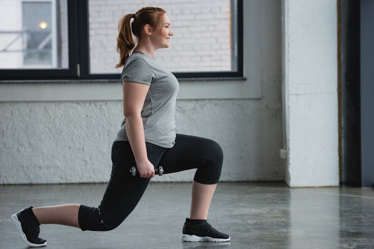 Woman performing lunges while holding dumbbells.