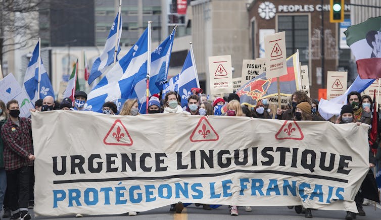 French-language rights protesters carry a banner that reads Urgence Linguistique and carry fleur de lis flags.
