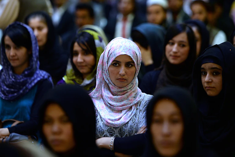 Women, most in hijab, stand in a crowd and listen attentively.