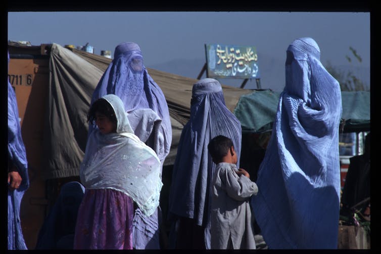 Veiled women and some children stand on the street