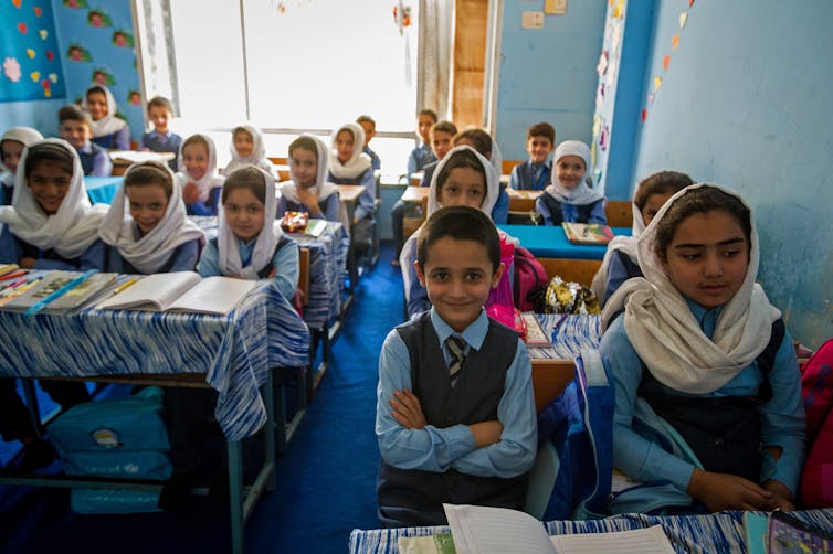 Sunny, blue-painted classroom full of smiling Afghan boys and girls