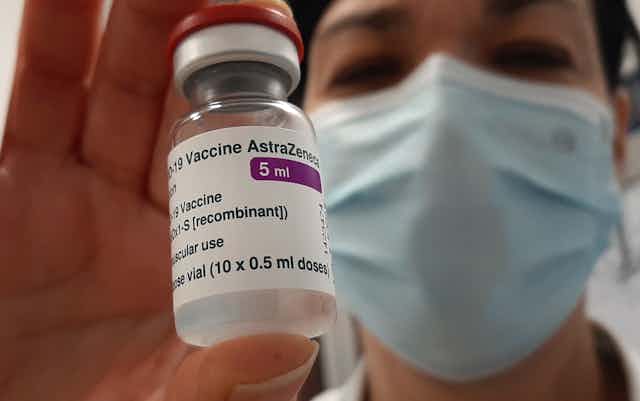Masked person holding a vial of AstraZeneca vaccine