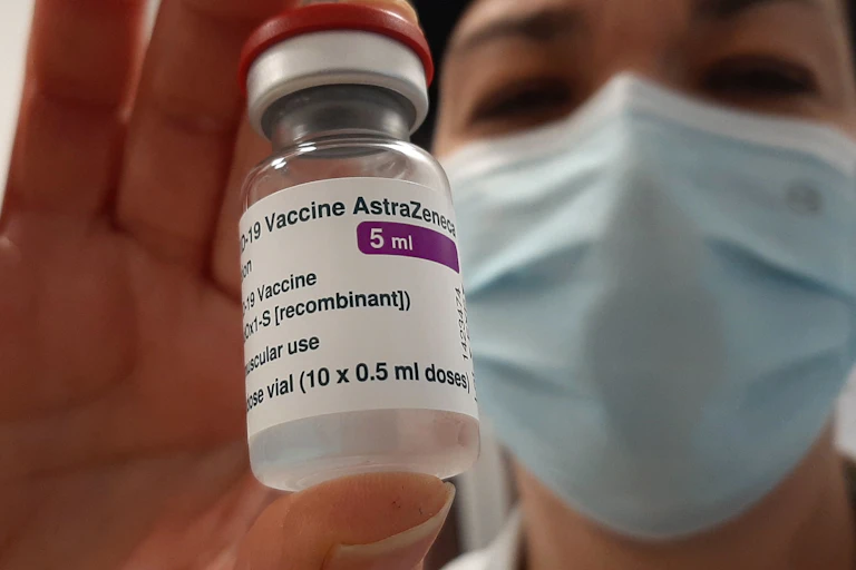 Masked person holding a vial of AstraZeneca vaccine