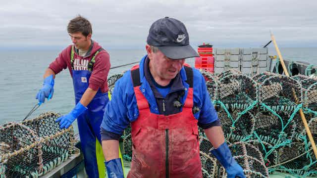 Two fishermen tend lobster traps on a boat.