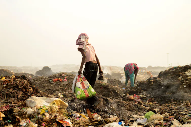 Two people pick through refuse at a huge dump site.