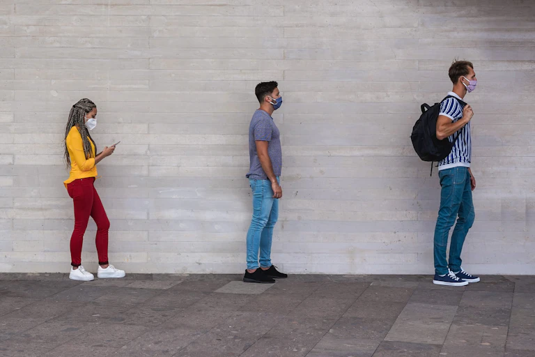 Four people wearing masks wait in a line.