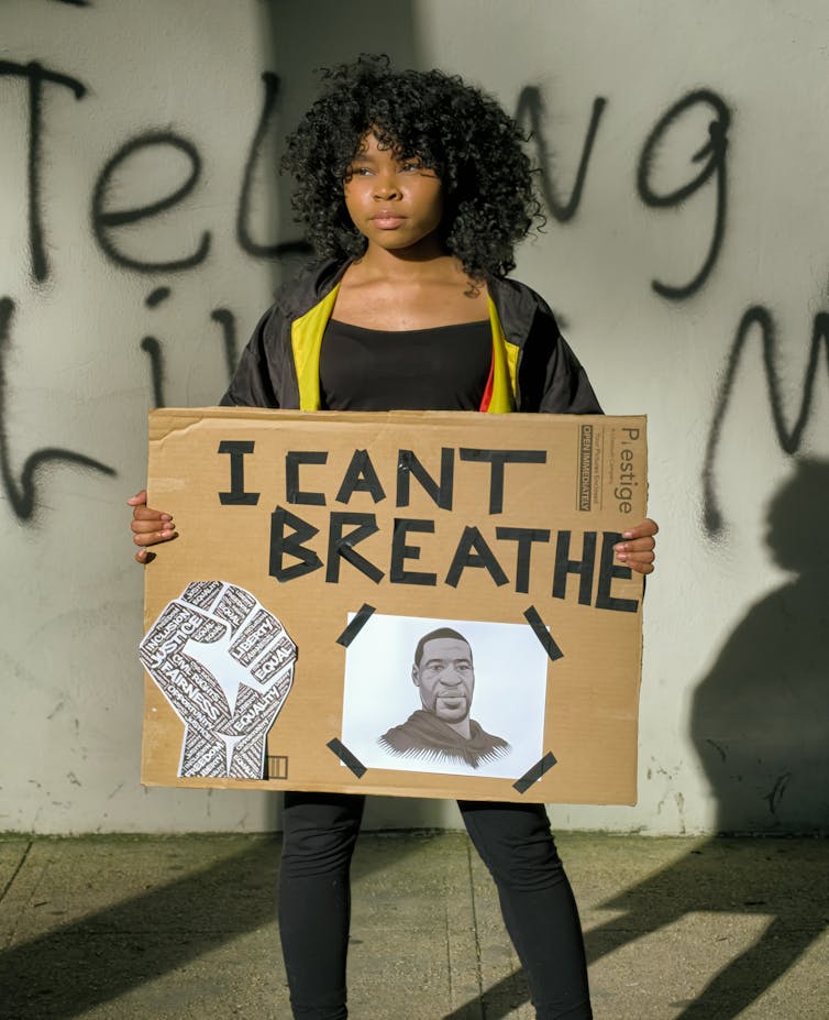 Une fille tient une pancarte en carton avec une photo de George Floyd et un texte qui dit « I CANT BREATHE »