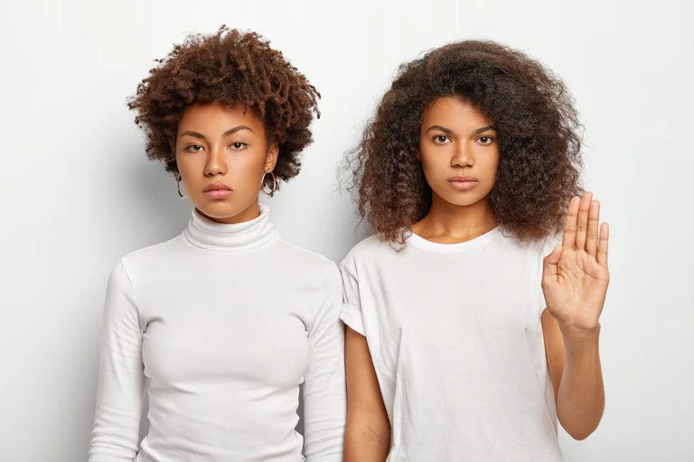 Two girls standing, one had her hand up in a stop gesture