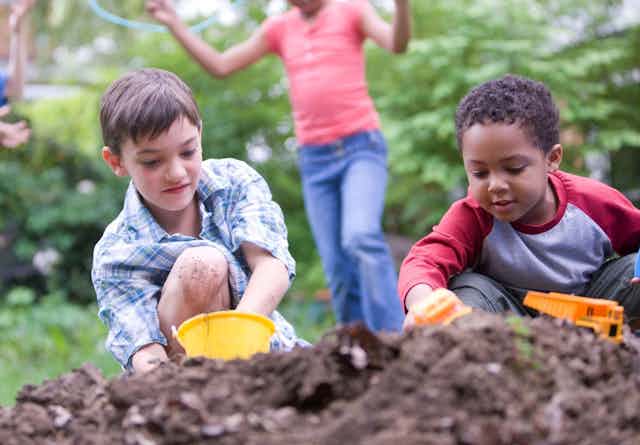 Two children playing with toys in a pile of dirt while two other kids play in the background