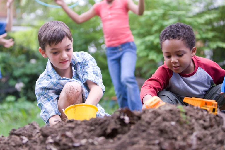 Two children playing with toys in a pile of dirt while two other kids play in the background