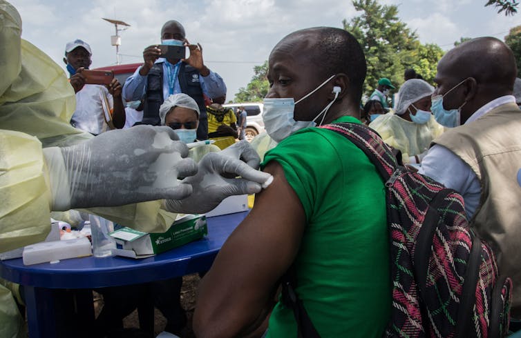 masked man's arm is prepped for injection outdoors