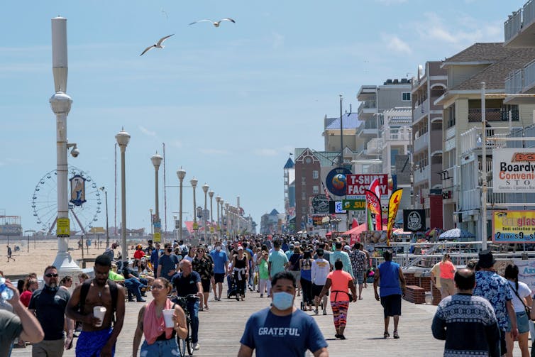 Vistors, many without masks, walk the beachfront boardwalk