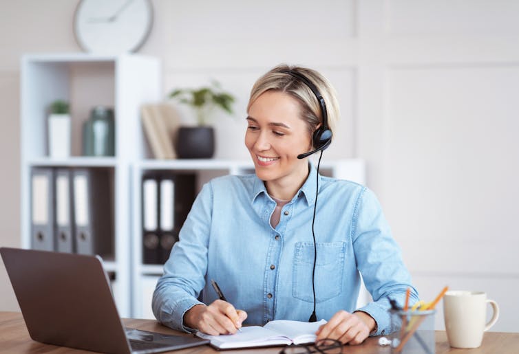 smiling women takes notes as she chats with colleagues online