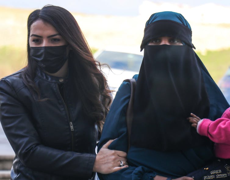 Police woman in mask holding arm of woman with face covered