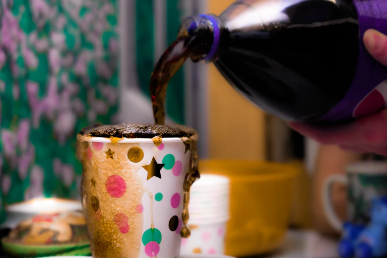 An overflowing cup of soda, with more being poured in from a bottle
