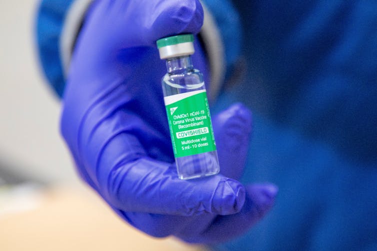 A hand in a purple glove holding a vial of vaccine