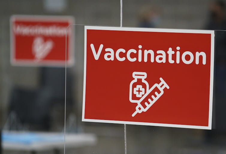 Red sign reading 'Vaccination' with an illustration of a syringe and a vial