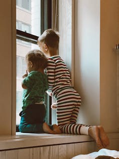 Two children on a windowsill looking outside at a tall building.