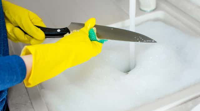 Persona con guantes amarillos lavando un de cuchillo de cocina.
