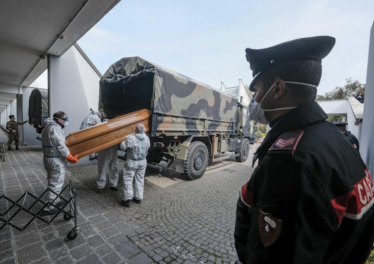 Italian troops load a coffin in to the back of a military vehicle.