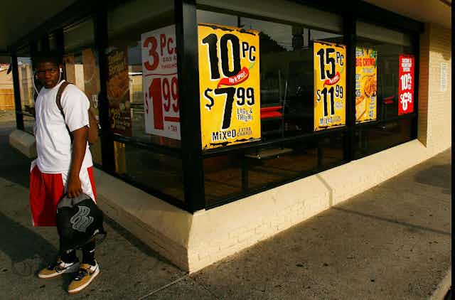 A boy stands next to a fast-food restaurant.