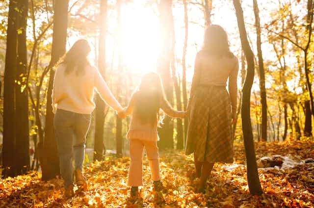Dos mujeres pasean con una niña de la mano por un bosque otoñal.